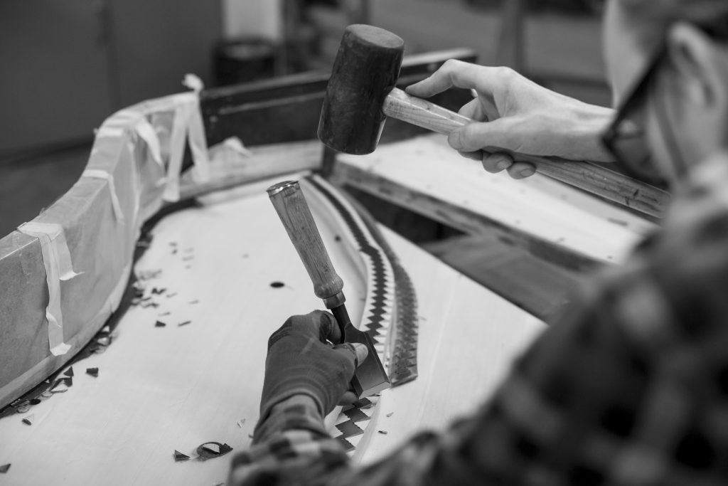 Working on the bridge caps of a grand piano with chisel and mallet – SAP Renovation.